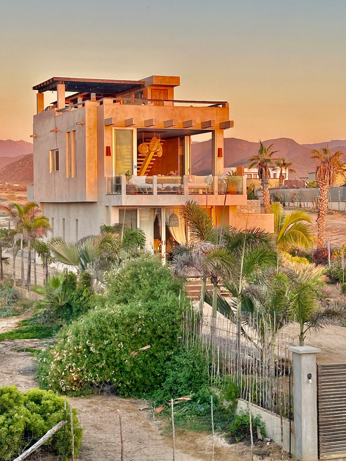 Ocean-facing side of the house in warm evening light, with the Sierra de la Laguna behind it